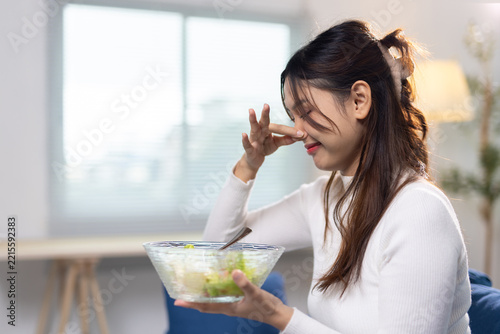Young woman pinching nose avoiding bad smell. Young Asian woman holding a salad bowl, pinching her nose, avoiding an unpleasant smell or healthy food she dislikes.
