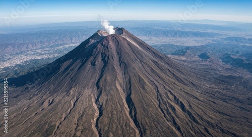 Aerial view of a majestic, gray volcano emitting white smoke against a clear blue sky