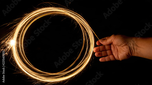 Hand holding glowing sparkler forming circular light trail against black background at night
