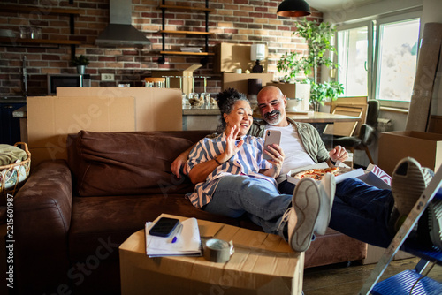 Couple video chatting on sofa surrounded by moving boxes