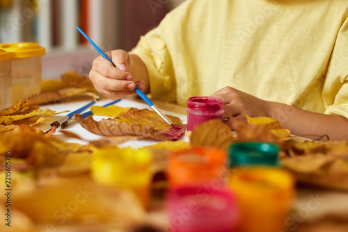 Child painting autumn leaves with vibrant gouache paints