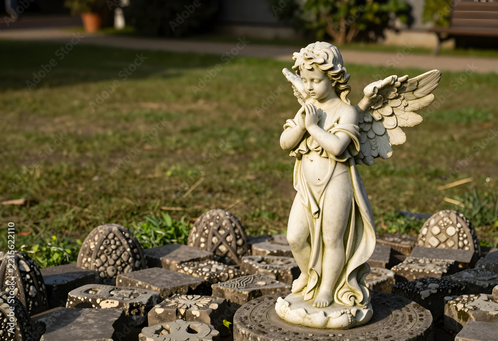 Fototapeta premium Spirituality and peace, stone angel statue praying in a garden setting with decorative paving stones for memorial or religious design concepts