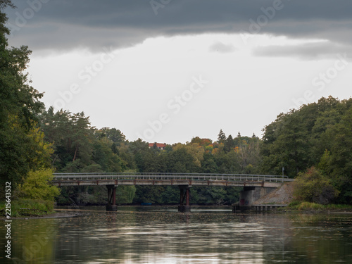 Old bridge spans calm water, surrounded by lush green trees