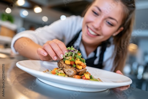 Chef smiles warmly as she garnishes a plated dish