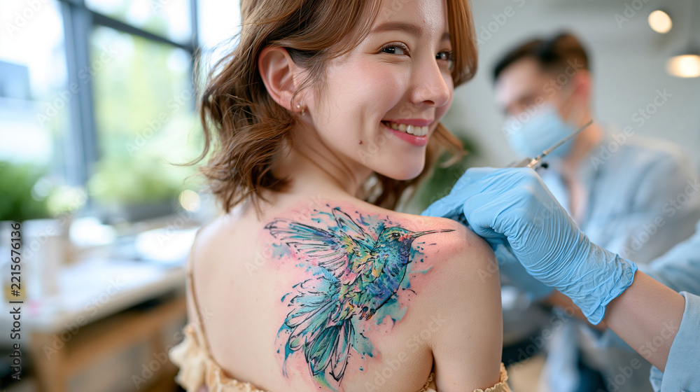 Fototapeta premium woman receiving a colorful hummingbird tattoo on her shoulder blade, close-up focus on the tattooed skin, bright airy tattoo studio, artist applying vibrant blue and green ink, detailed needlework, 