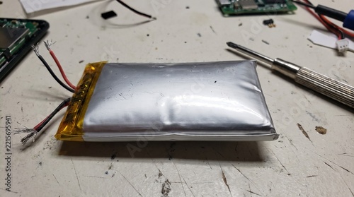 Swollen lithium polymer battery with exposed wires on a workbench for