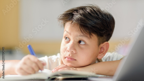 Distracted Asian boy daydreaming while doing homework with pen
