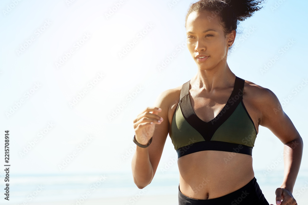 Naklejka premium Fitness, health and running with woman on beach for cardio training or morning workout. Blue sky, exercise and wellness with African athlete or runner on space outdoor for challenge or improvement