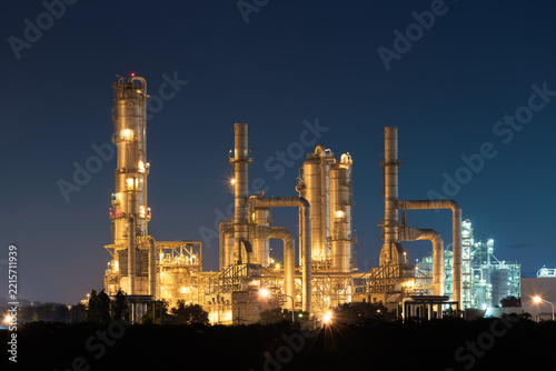 Illuminated petrochemical plant at Map Ta Phut, Rayong, Thailand, with process columns, interconnected pipes and steel platforms against dark blue night sky, highlighting industrial infrastructure.