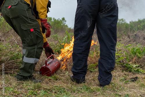 Workers performing a controlled burn with a torch in a rural field