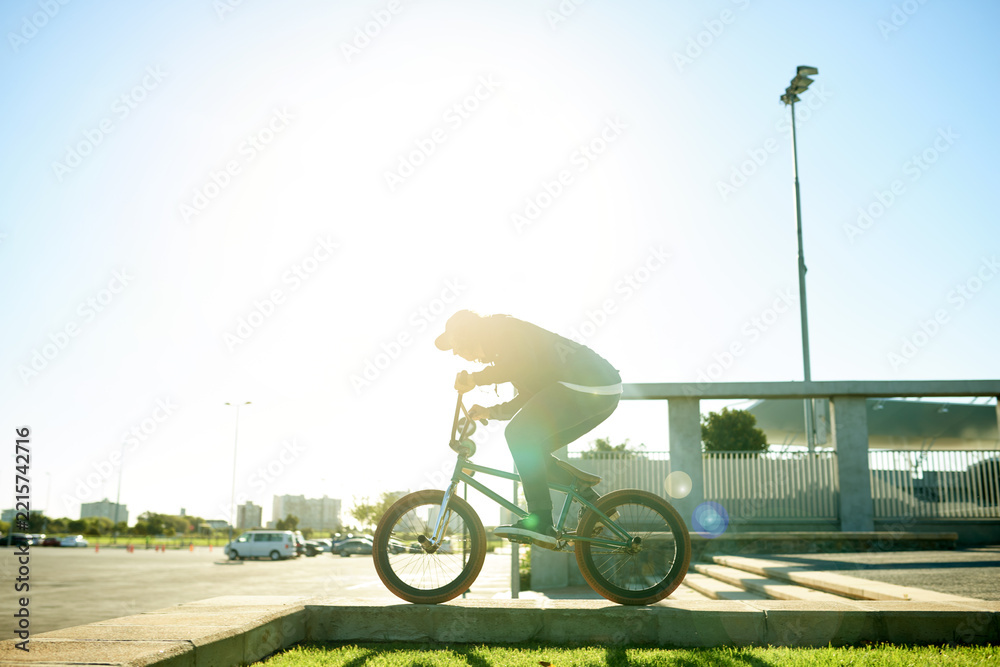 Naklejka premium BMX, man and bicycle in city for exercise, eco friendly travel and cycling with space. Person, riding bike and cyclist on curb outdoor for fitness, urban sports and balance for cardio with flare