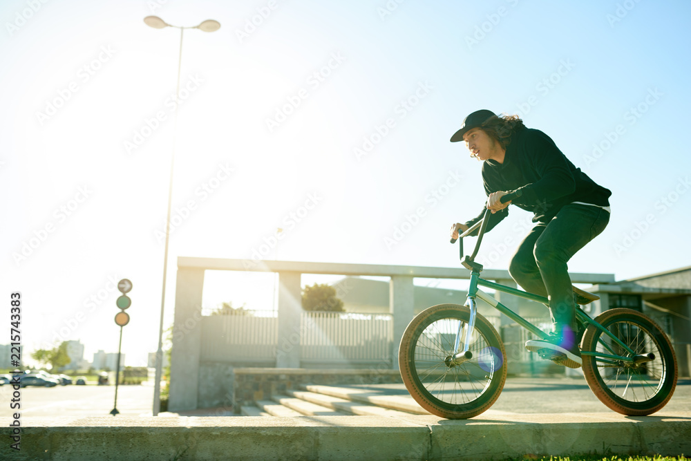 Naklejka premium BMX, man and bicycle in city for sports, urban challenge and exercise with space. Person, riding bike and cyclist on curb outdoor for fitness, extreme cycling and balance for stunt with flare