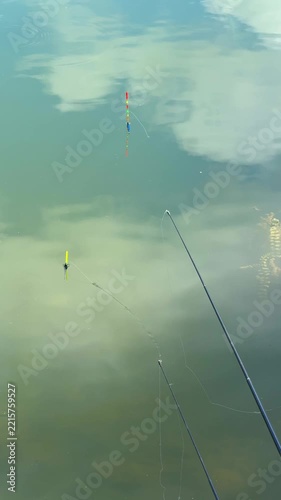Fishing rods and colorful floats wait for a bite in calm water. Recreational fishing represents outdoor leisure, patience and a traditional hobby