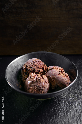 Rich chocolate ice cream scoops served in a black bowl on a dark textured surface, with negative space for advertising and copy