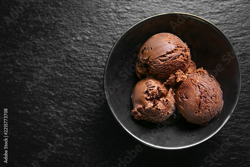 Rich chocolate ice cream scoops served in a black bowl on a dark textured surface, with negative space for advertising and copy