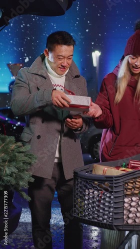Multi-cultural family young atrractive couple putting their presents into car back shopping for friends at the shopping mall. Nighttime. Winter sale. Holiday season.