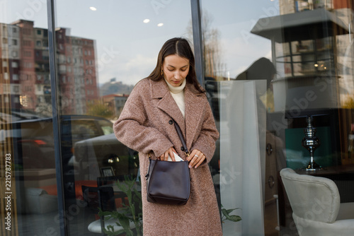Beautiful woman holding black leaver bag standing on city street near shopping center