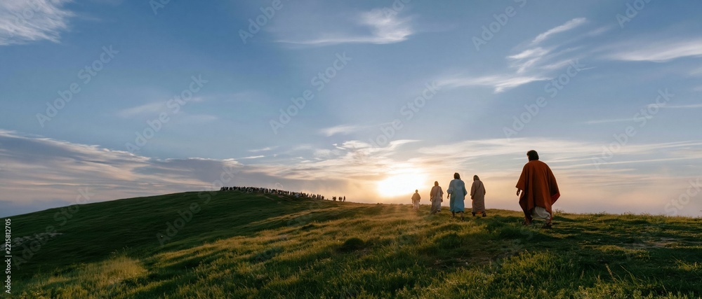Naklejka premium Jesus and his disciples walking up a grassy hill toward the sermon on the mount, with a soft glowing sky and copy space for church banners
