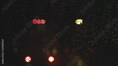 Blurry car traffic lights shining through a rainy window at night