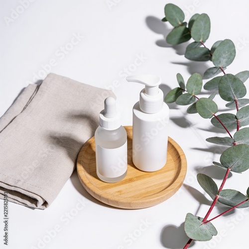 Cosmetic skincare bottles on a wooden tray with a linen cloth and eucalyptus