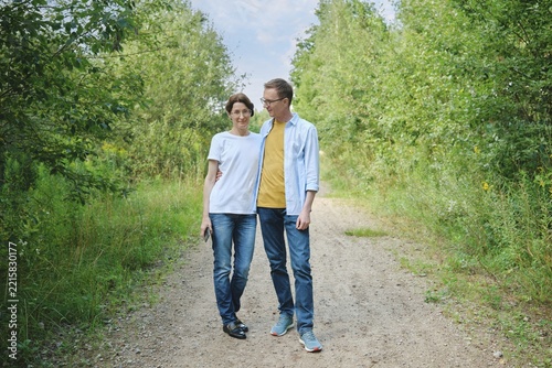 A middle-aged couple enjoys a stroll along a gravel path shaded by lush greenery. They smile at each other and have a leisurely conversation