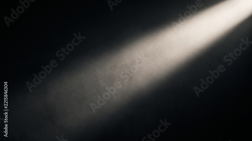 A single bright white spotlight beam diagonal across a dark black background with visible floating dust particles in the atmospheric light ray