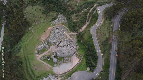 Aerial view of the Q'enqo archaeological site with limestone rock formations, ancient stone structures, and green hills, next to a winding road in Cusco, Cusco, Peru.
