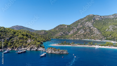 Aerial view of the turquoise waters of the Blue Lagoon in Oludeniz, surrounded by lush green mountains, sandy beaches, and anchored boats in Oludeniz, Mugla, Turkiye.