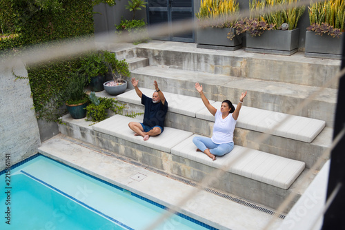 Mature African American couple stretching and breathing on padded cushions on tiered steps by pool