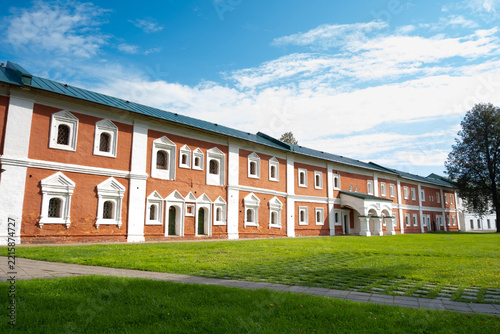 A historic building made of red bricks stands in a grassy area. The sky is clear with some clouds.