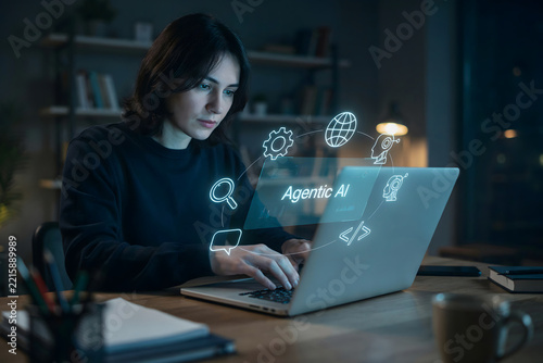 A woman working on a laptop at a desk with a glowing blue holographic display showing the text agentic ai and various digital tech