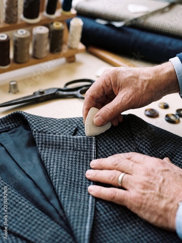 Hands of a professional tailor marking wool fabric with chalk while tailoring a custom bespoke suit jacket in workshop