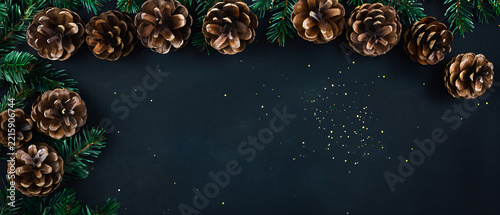 Christmas background with pine cones and fir branches on a dark blackboard surface with gold glitter