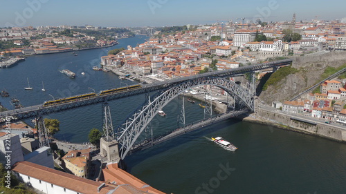 Aerial view of Luis I Bridge spanning the Douro River with a train on the upper deck and a boat below, surrounded by the historic cityscape of Porto, Porto District, Portugal.