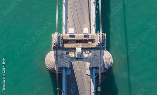 Aerial view of the historic stone suspension bridge with a dedicated cycling lane crossing the turquoise waters of the Rhone River in La Voulte-sur-Rhone, Auvergne-Rhone-Alpes, France.