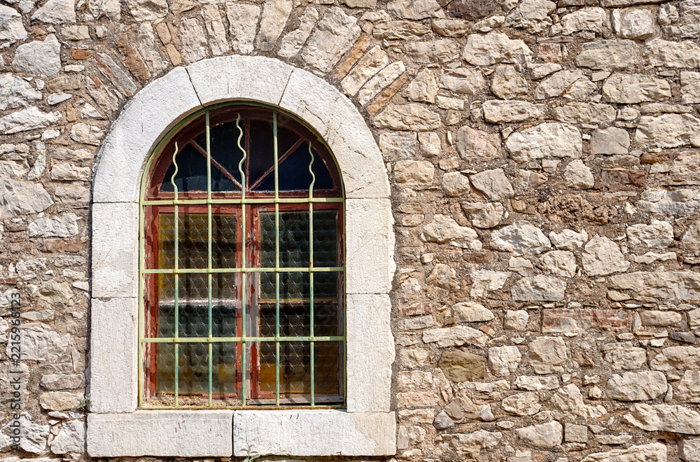 Obraz premium Single barred round arch window set in light, irregular stone wall, Patras, Greece