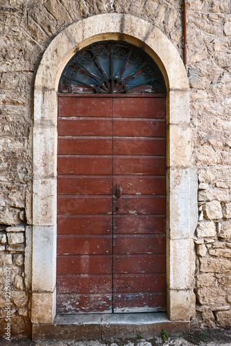 Dark red wooden door with wrought iron transom window set within rounded stone archway entrance, Patras, Greece