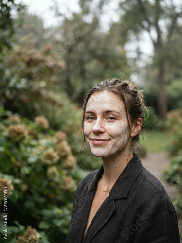 Smiling woman in a dark blazer wearing a thick white face mask in a park