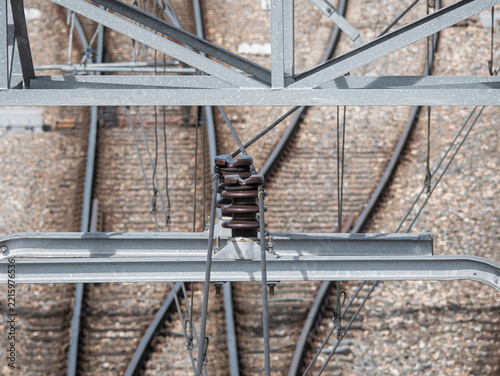 Messenger wire suspension assembly securing the messenger wire to the overhead contact line bracket of the catenary system above a railway station turnout