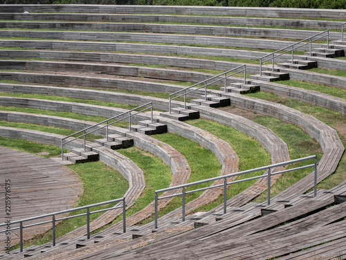 View of the open-air amphitheater in Madrid's Manzanares Linear Park, featuring curved tiered seating with wooden benches and interspersed green spaces, as well as staircases with railings