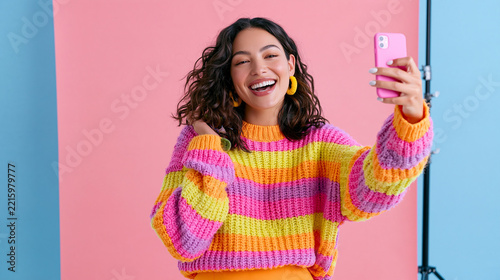 Joyful young woman taking a selfie in a colorful sweater against vibrant backgrounds.
