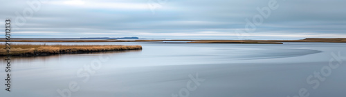 Calm water and golden grass banks beneath an overcast sky