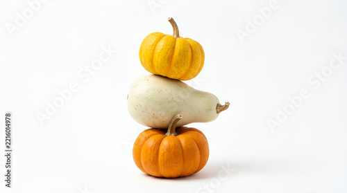 Three mini pumpkins balanced in a vertical stack on a clean, minimalist white surface against a plain white background.