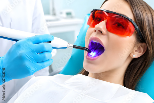 Dentist using dental curing light to harden composite filling on patient tooth