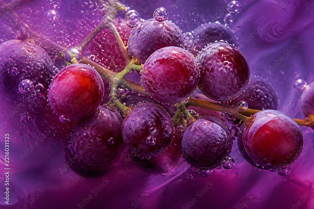 Naklejka premium Clusters of purple grapes covered in water droplets are suspended against a vibrant, swirling magenta background.