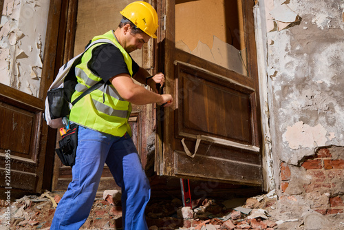 Construction laborer utilizes pry bar to reposition ancient door