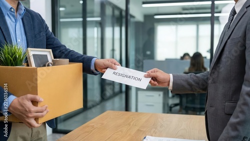 Employee giving a resignation letter and cardboard box to manager in modern office