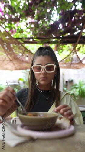 Young woman eating at outdoor garden table beneath leafy trellis