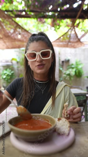Woman tasting red soup with a spoon at a shaded garden cafe table