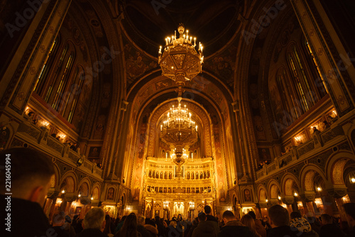 View of the ornate interior of the Timisoara Orthodox Metropolitan Cathedral with glowing chandeliers and religious iconography above a congregation in Timisoara, Timis, Romania.